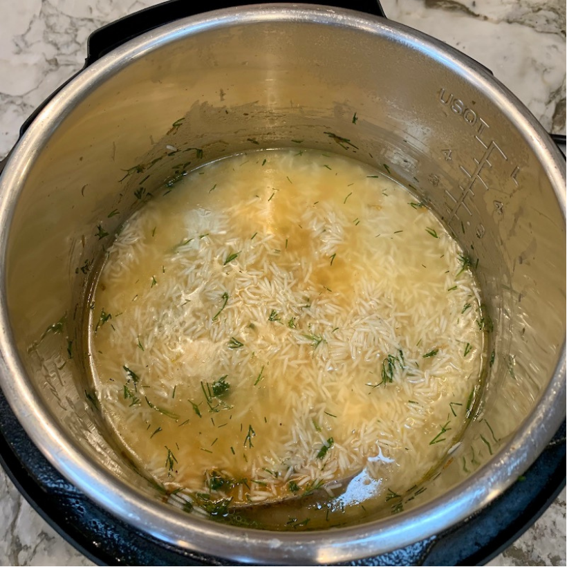 Uncooked rice, broth, and herbs in an Instant Pot on a marble countertop, ready to be cooked.