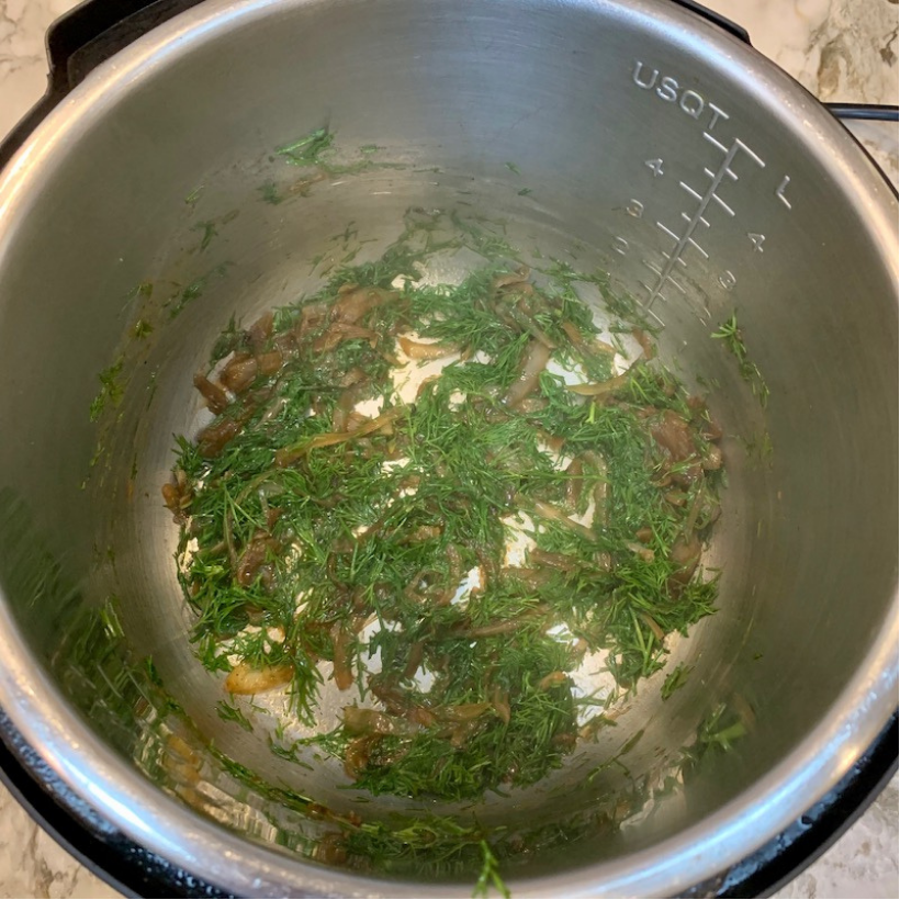 Sautéed onions and fresh dill in the bottom of a stainless steel Instant Pot, with visible spatters on the sides and measurement markings inside the pot.