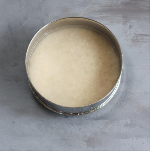 A metal bowl filled with uncooked rice soaking in cloudy water, placed on a gray surface.