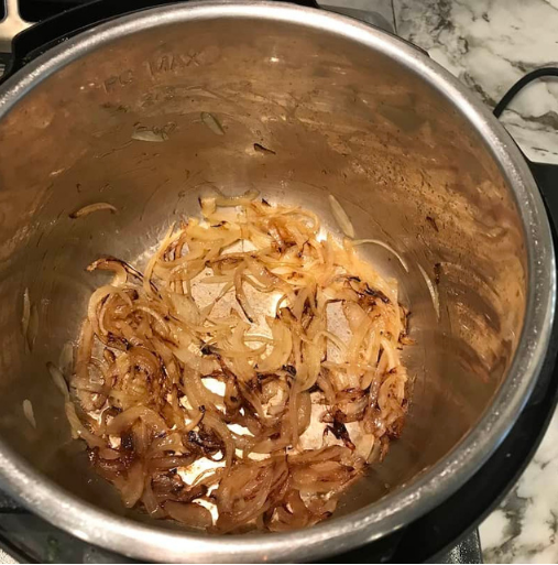 Thinly sliced onions are sautéed and partially caramelized at the bottom of a stainless steel pot on a marble countertop.
