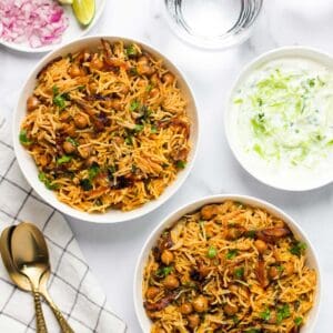chickpea biryani served in two white bowls with raita on the side