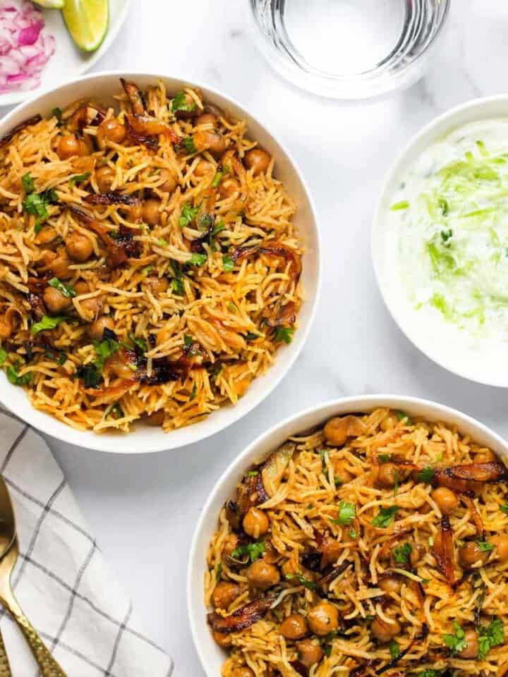 chickpea biryani served in two white bowls with raita on the side