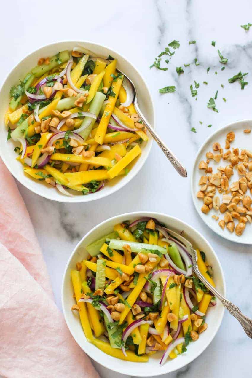 Mango salad in 2 white bowls with peanuts on the side 