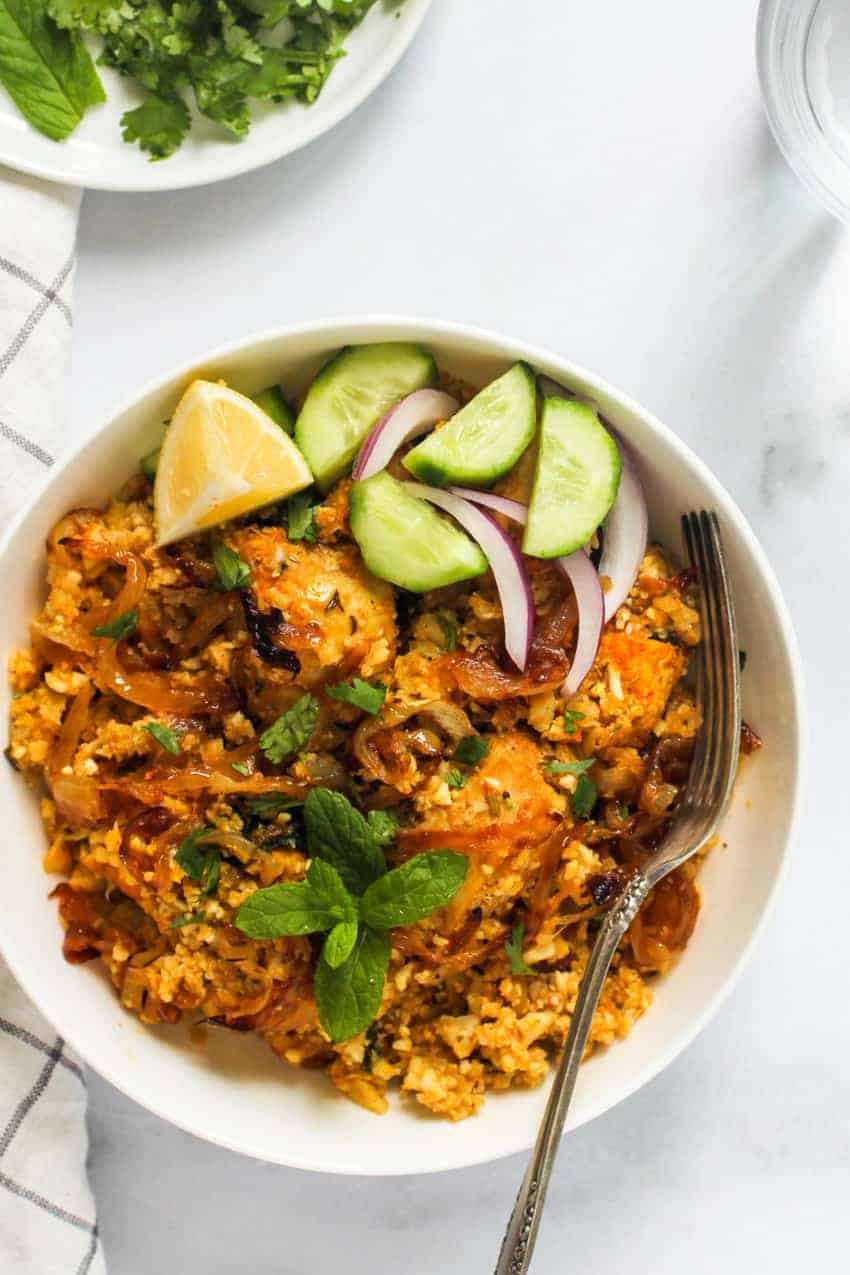 cauliflower rice biryani with lemon wedge, sliced cucumber and onion