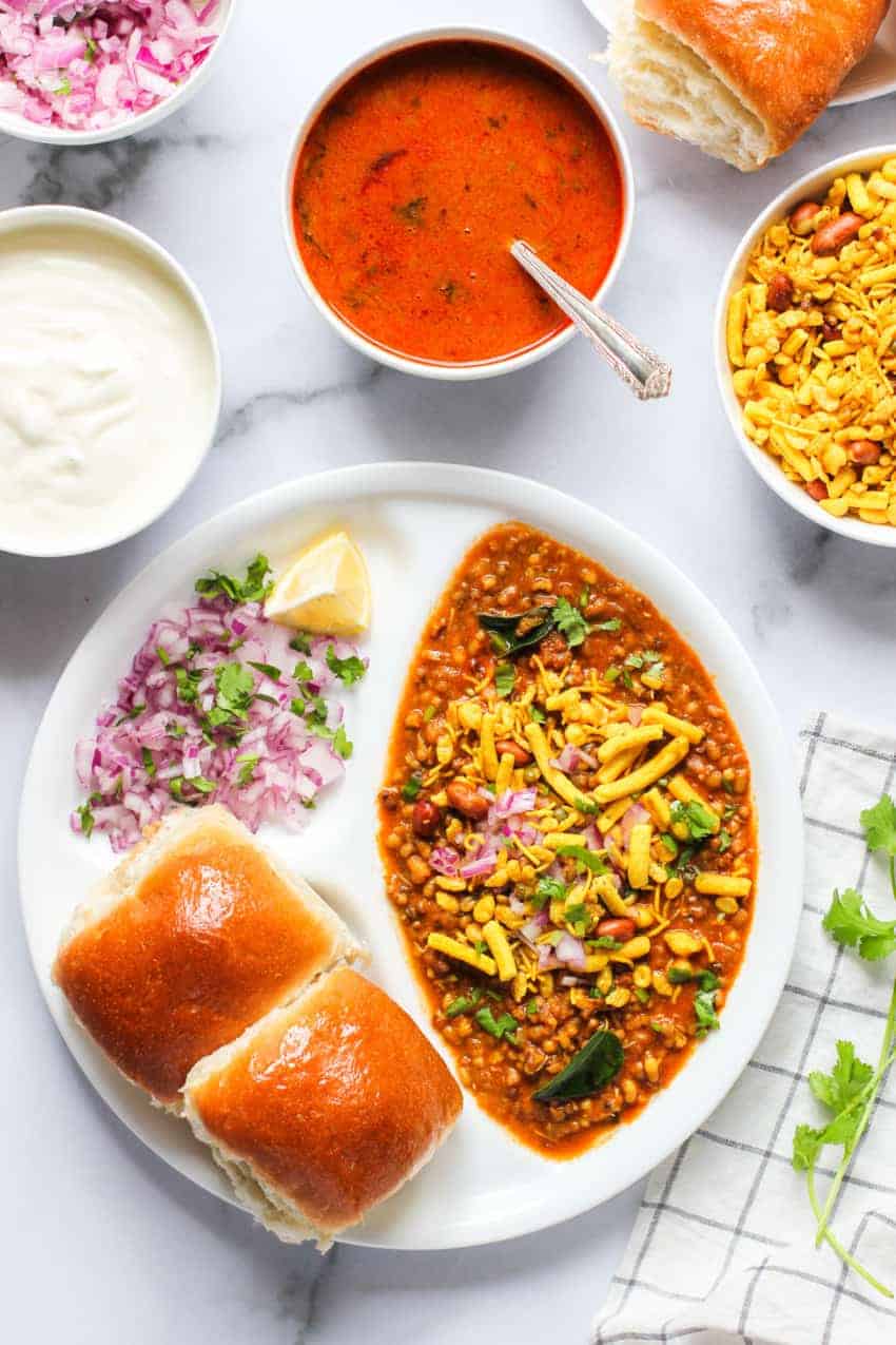 Misal Pav served in a white plate with toppings places on the side  