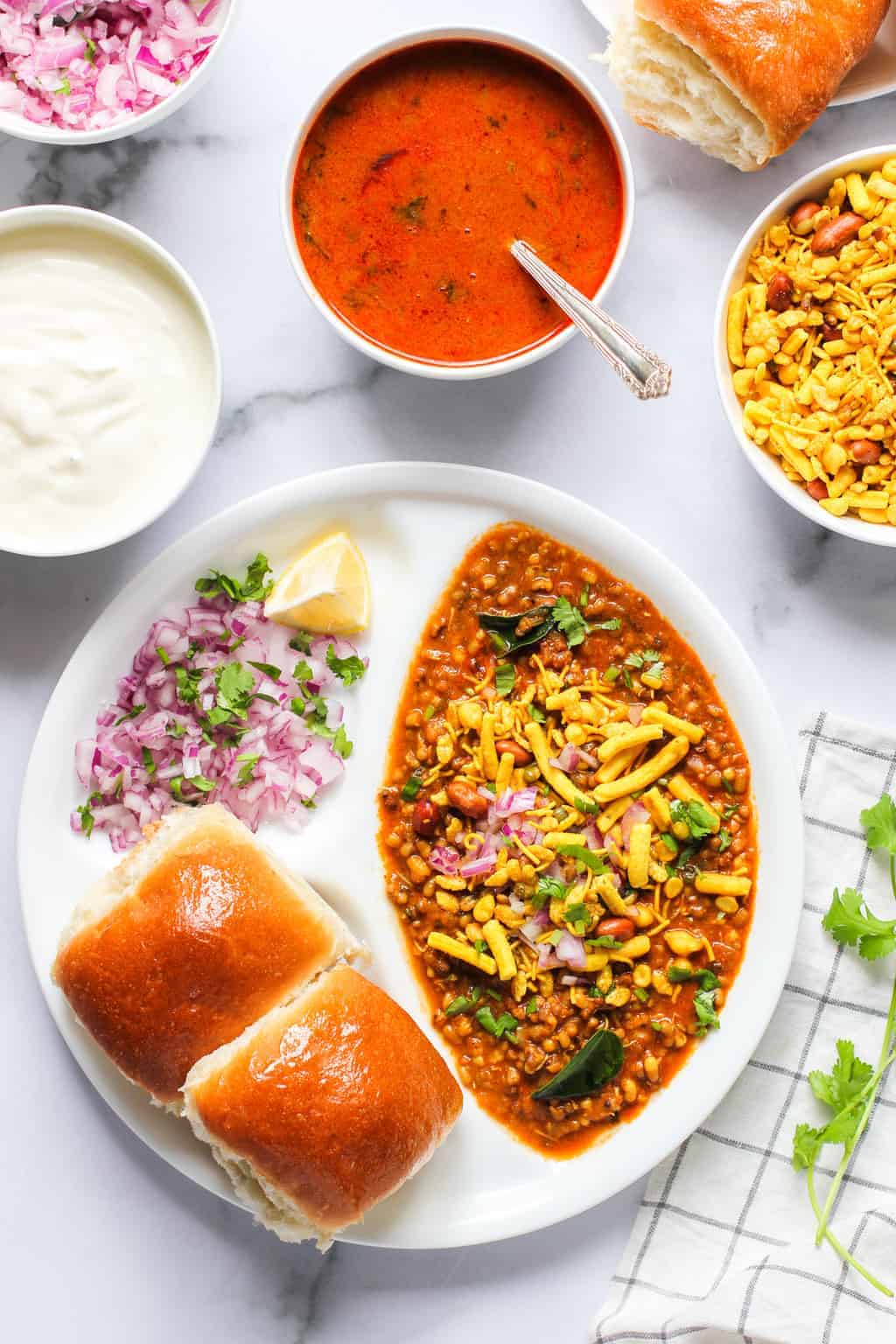 Misal Pav served in a white plate with all the garnish ingredients on the sides