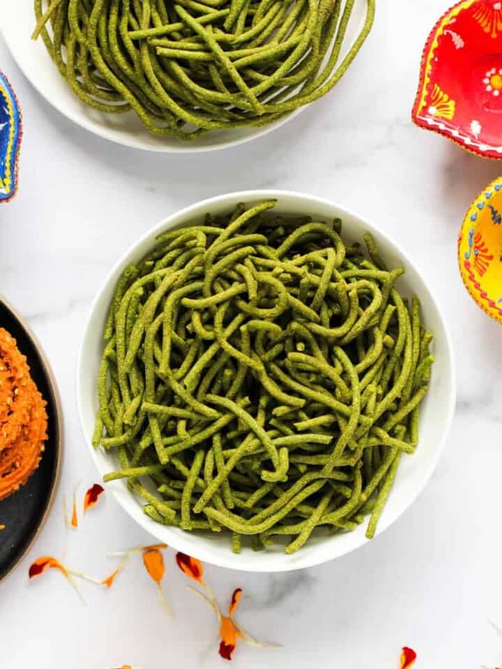 spinach sev in a bowl with other diwali snacks on the side