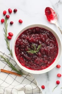 Cranberry sauce in a white bowl with rosemary and cinnamon on the side