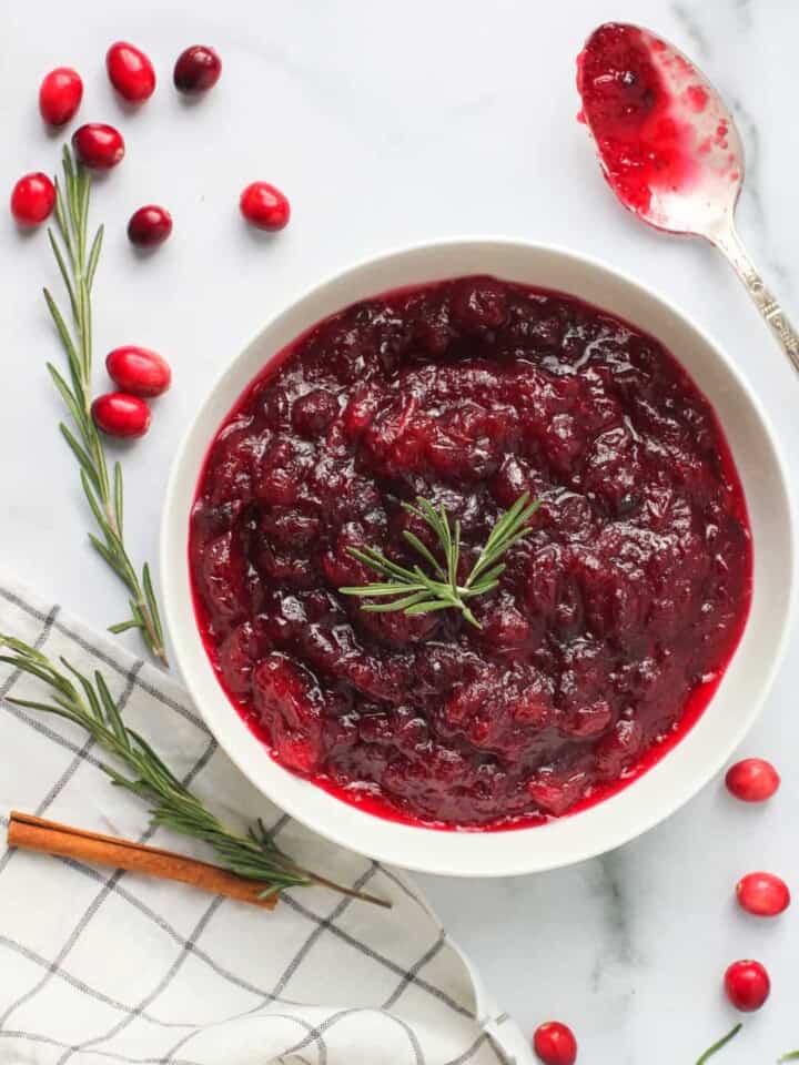 Cranberry sauce in a white bowl with rosemary and cinnamon on the side