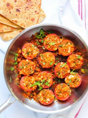 stuffed tomatoes in a frying pan with parathas on the side