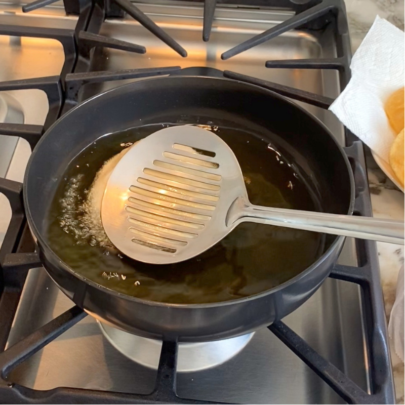 A metal slotted spoon lifts presses the puri in hot oil.