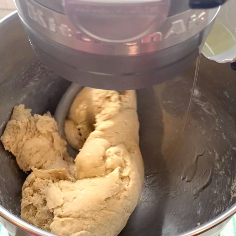 A stand mixer kneads a large ball of bread dough in a stainless steel mixing bowl.