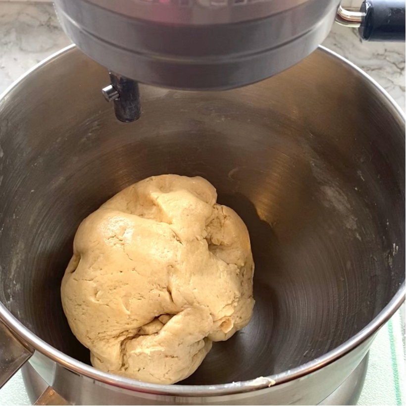 A ball of dough sits in the bowl of a stand mixer on a kitchen counter.