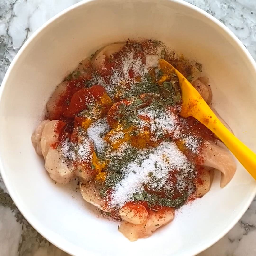 chicken with marination spices in a white bowl.