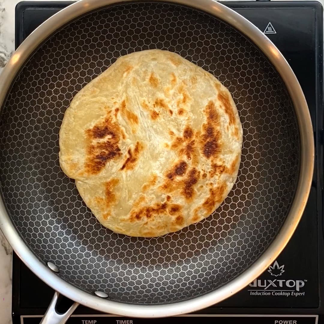 Cooked frozen paratha on a non stick pan.