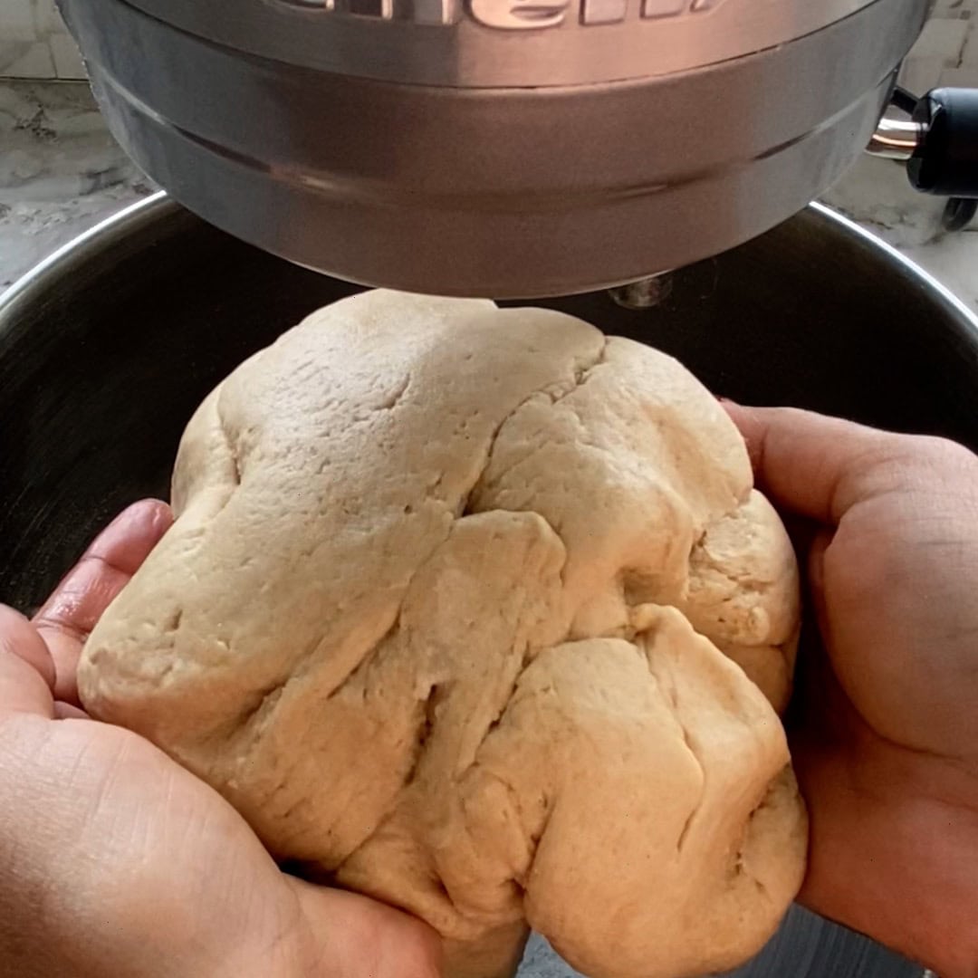 A person holds a ball of dough in both hands over a stand mixer bowl.