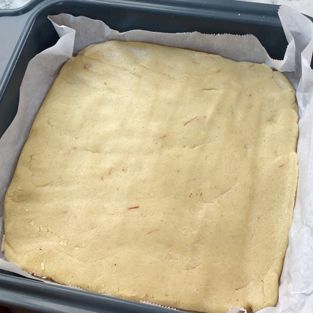 A square baking pan lined with parchment paper, filled with an even layer of dough.