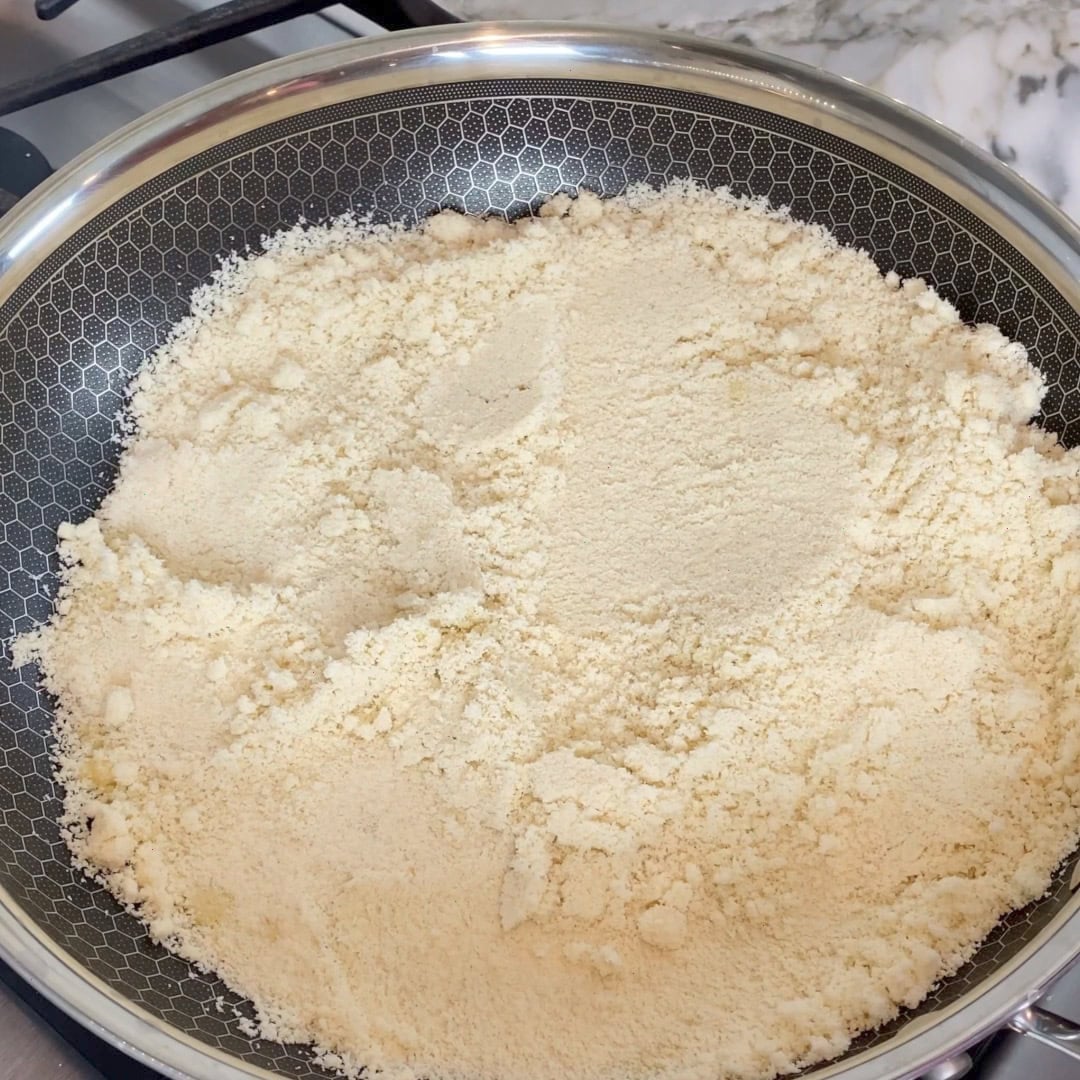 A frying pan filled with almond flour sits on a stovetop, ready for toasting.