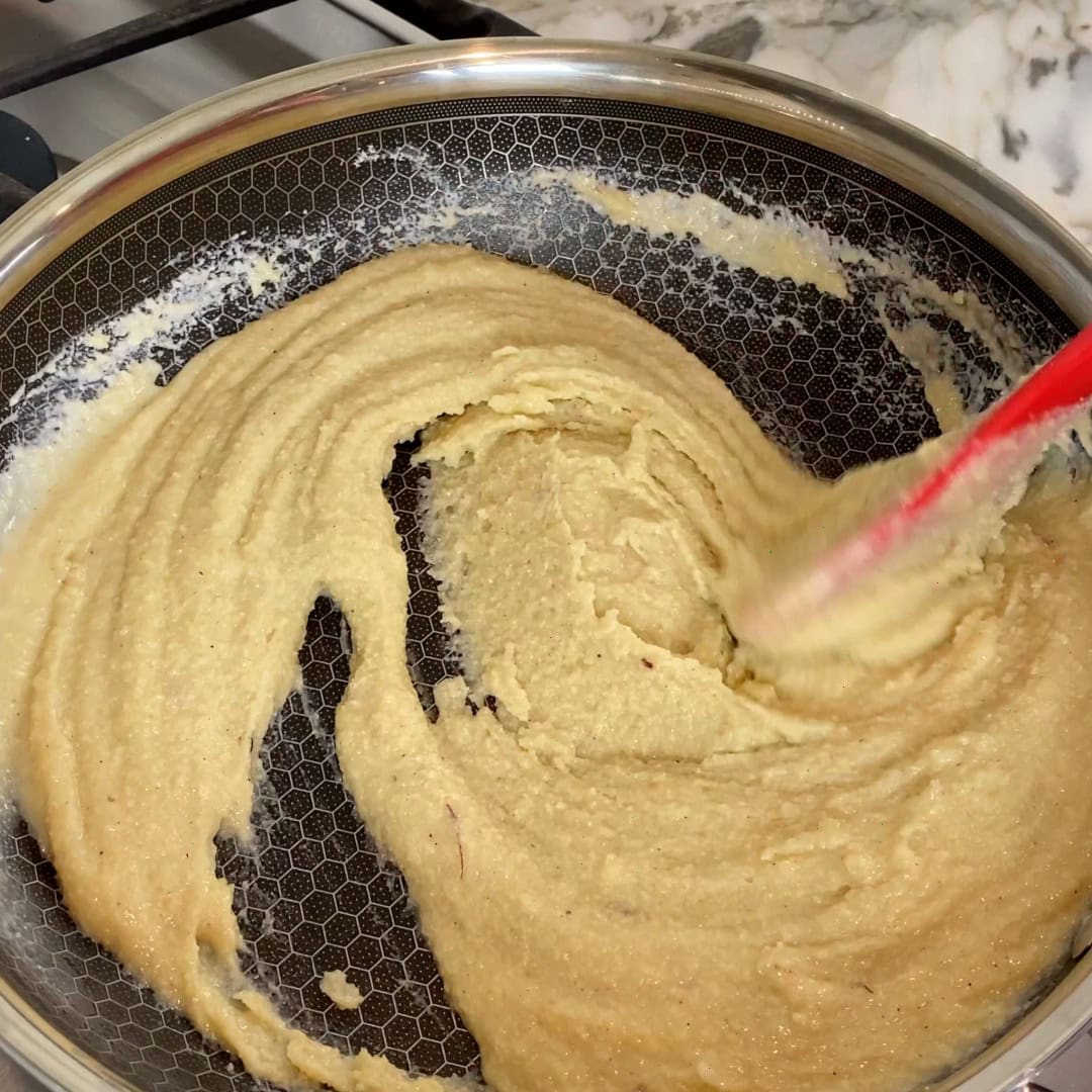 A red spatula stirs thick, light brown batter or dough in a nonstick pan on stove.