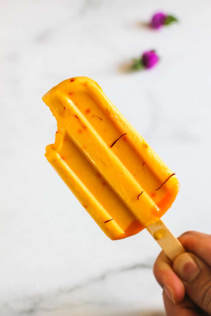 one mango lassi popsicle with a bite taken out of it