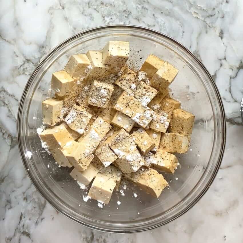 tofu cubes in a bowl with salt, pepper and corn starch 