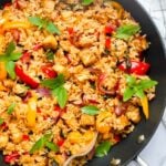 A skillet filled with Thai basil fried rice, tofu, bell peppers, and fresh basil, with a serving spoon placed inside. Text overlay: Easy Thai Basil Fried Rice vegan recipe.