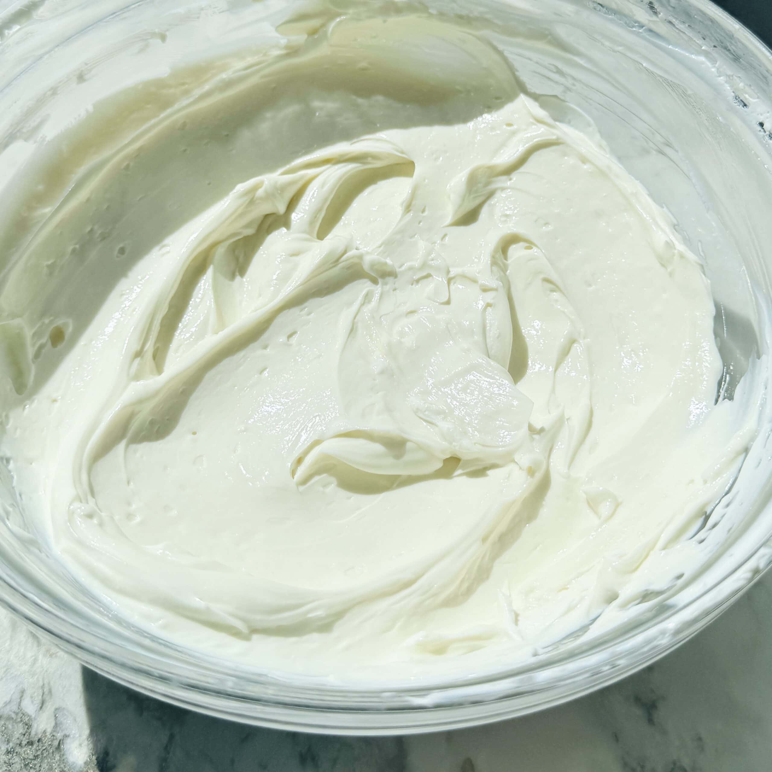 A clear glass bowl filled with smooth, creamy white yogurt.