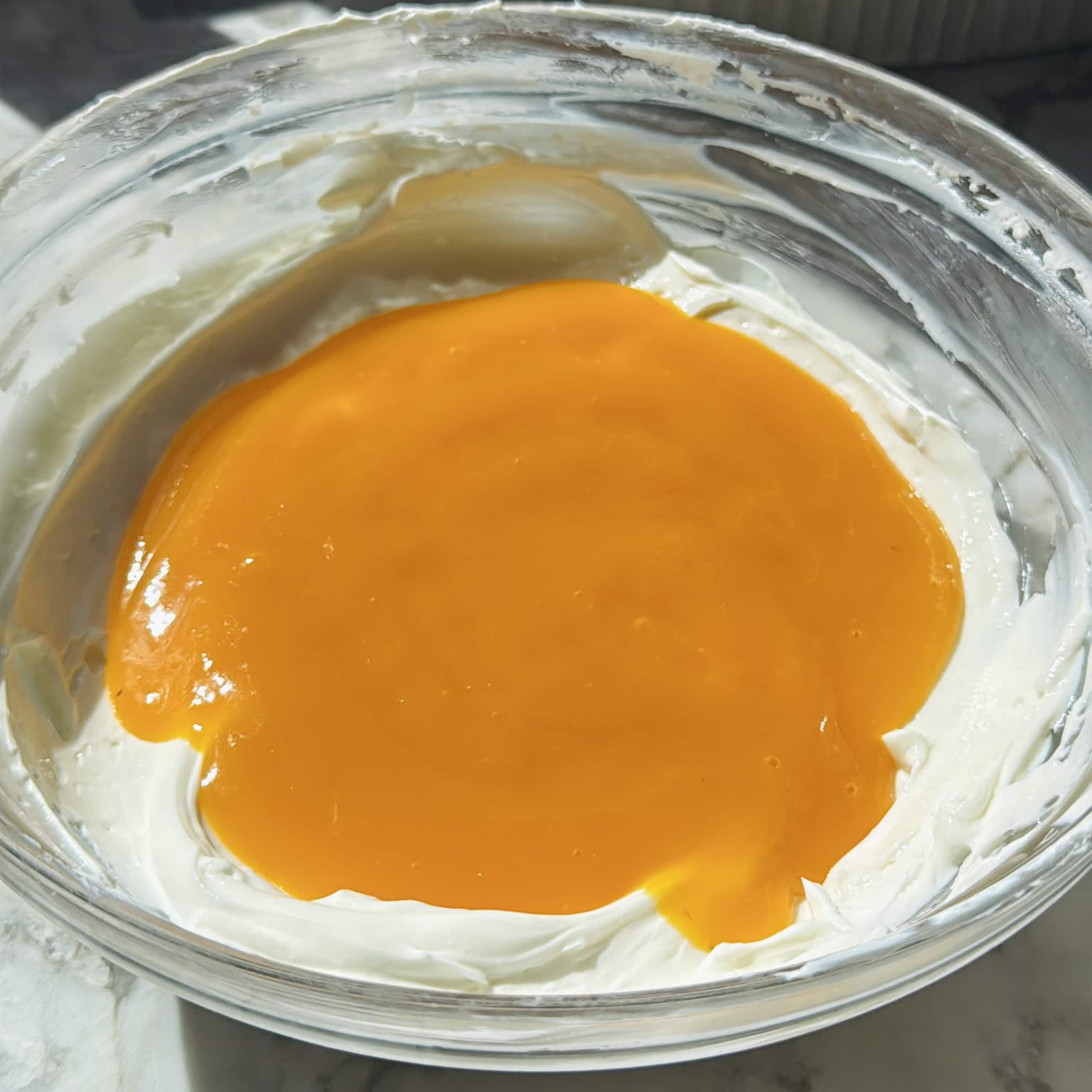 A glass bowl containing creamy yogurt with a layer of bright orange mango puree on top.