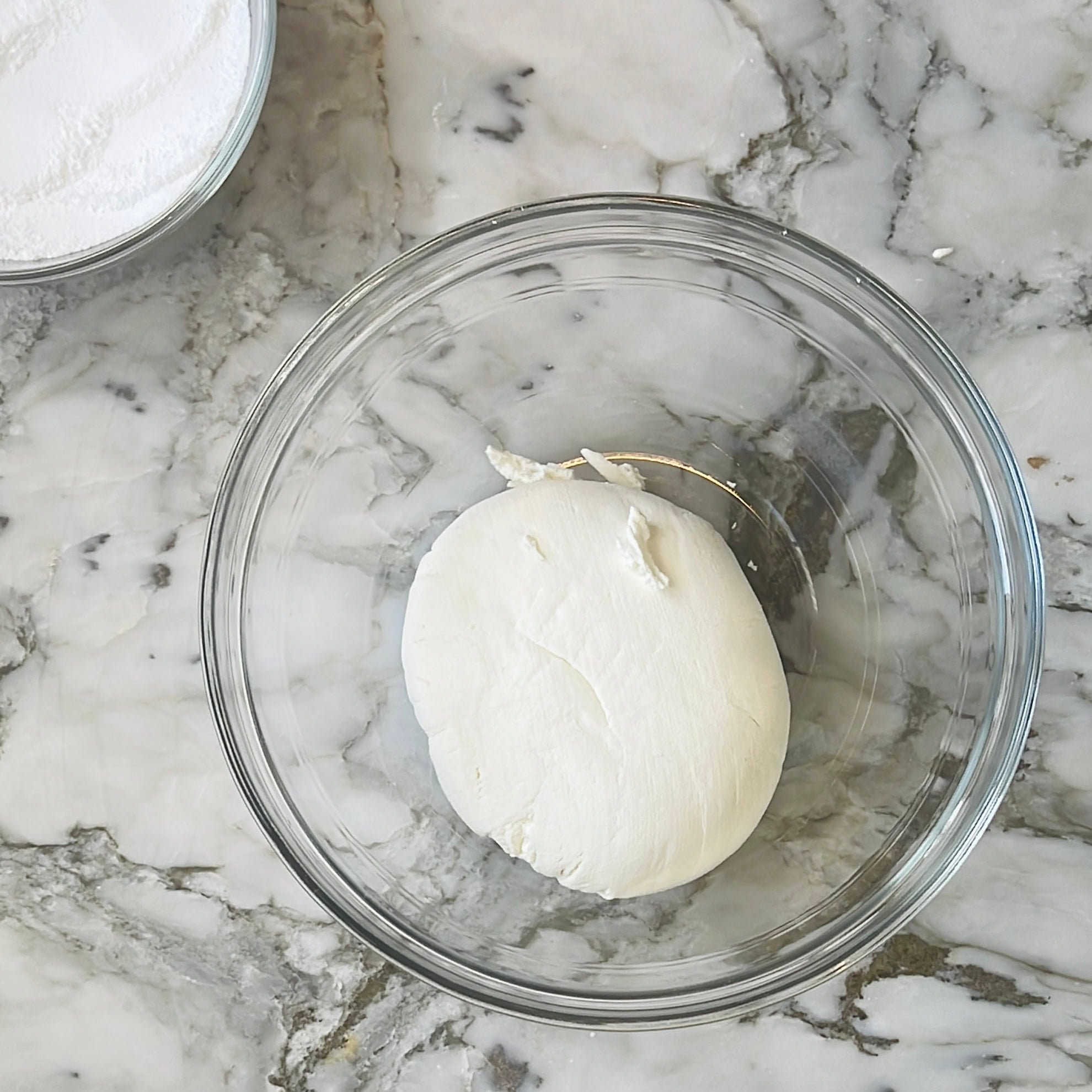 A ball of thick strained yogurt in a clear glass bowl on a marble countertop.