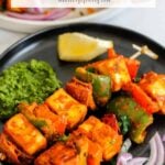 A black plate with skewered paneer tikka, green chutney, sliced red onions, and a lemon wedge. The caption above reads The Best Paneer Tikka (Air Fryer, Oven or Grill).