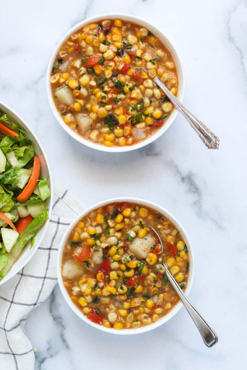 corn poblano soup on two bowls with a salad 