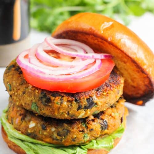 stacked burger patties on buns with lettuce, tomato and onion