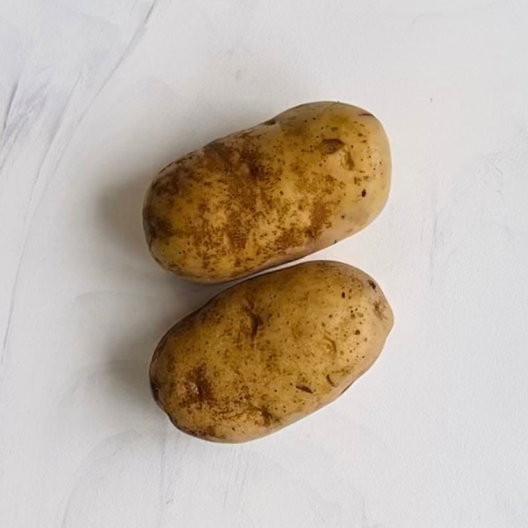 Two unpeeled russet potatoes with dirt on their skins placed on a white surface.