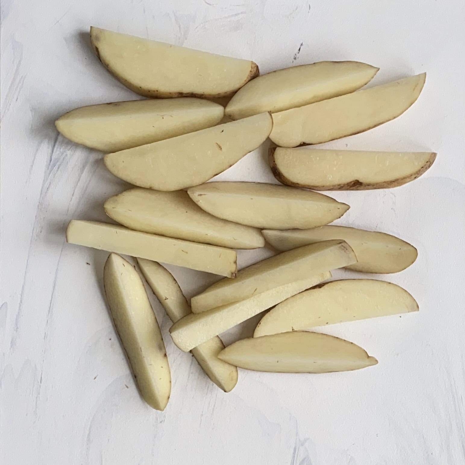 A pile of raw potato wedges arranged on a white surface.
