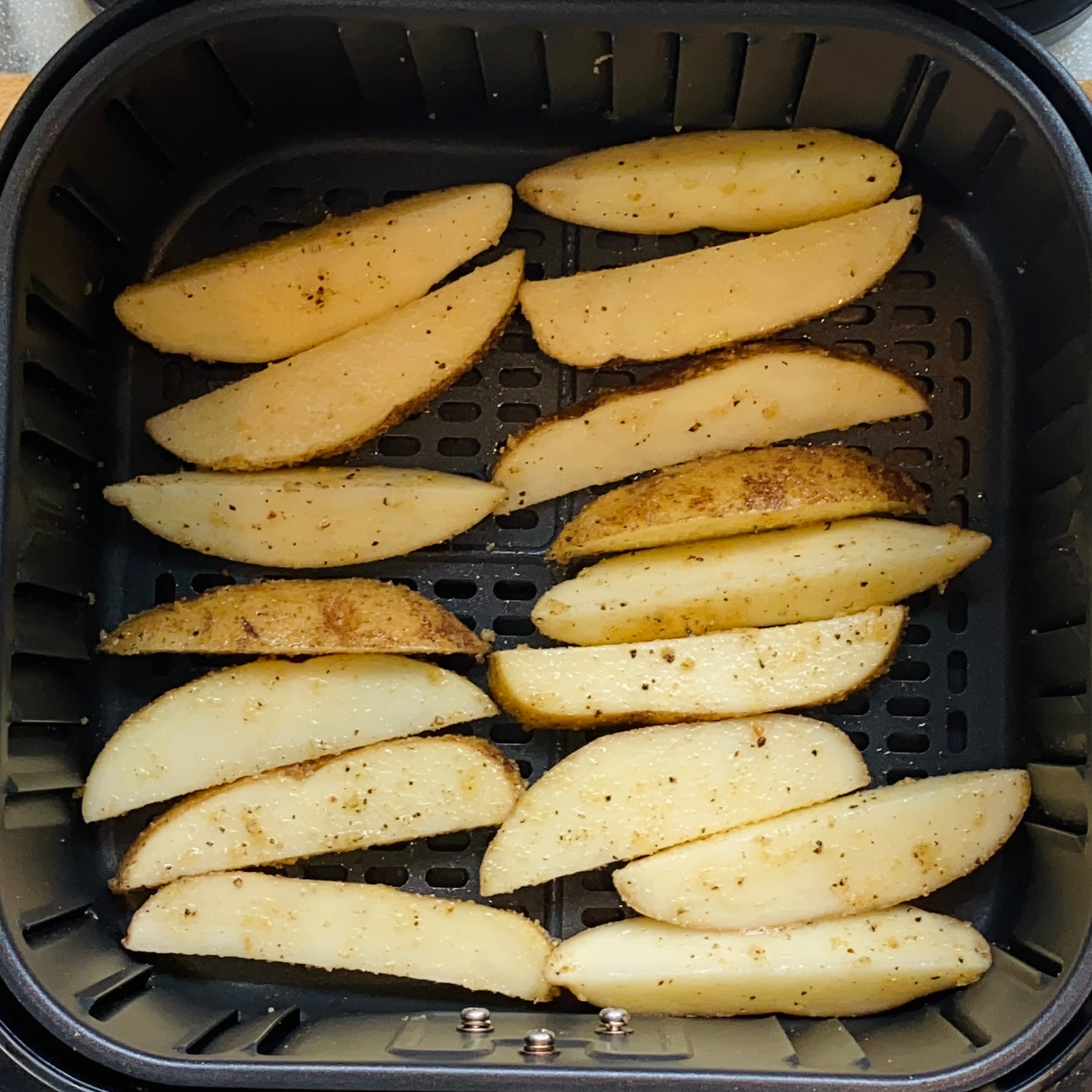 Seasoned potato wedges arranged in a single layer inside an air fryer basket, ready to be cooked.