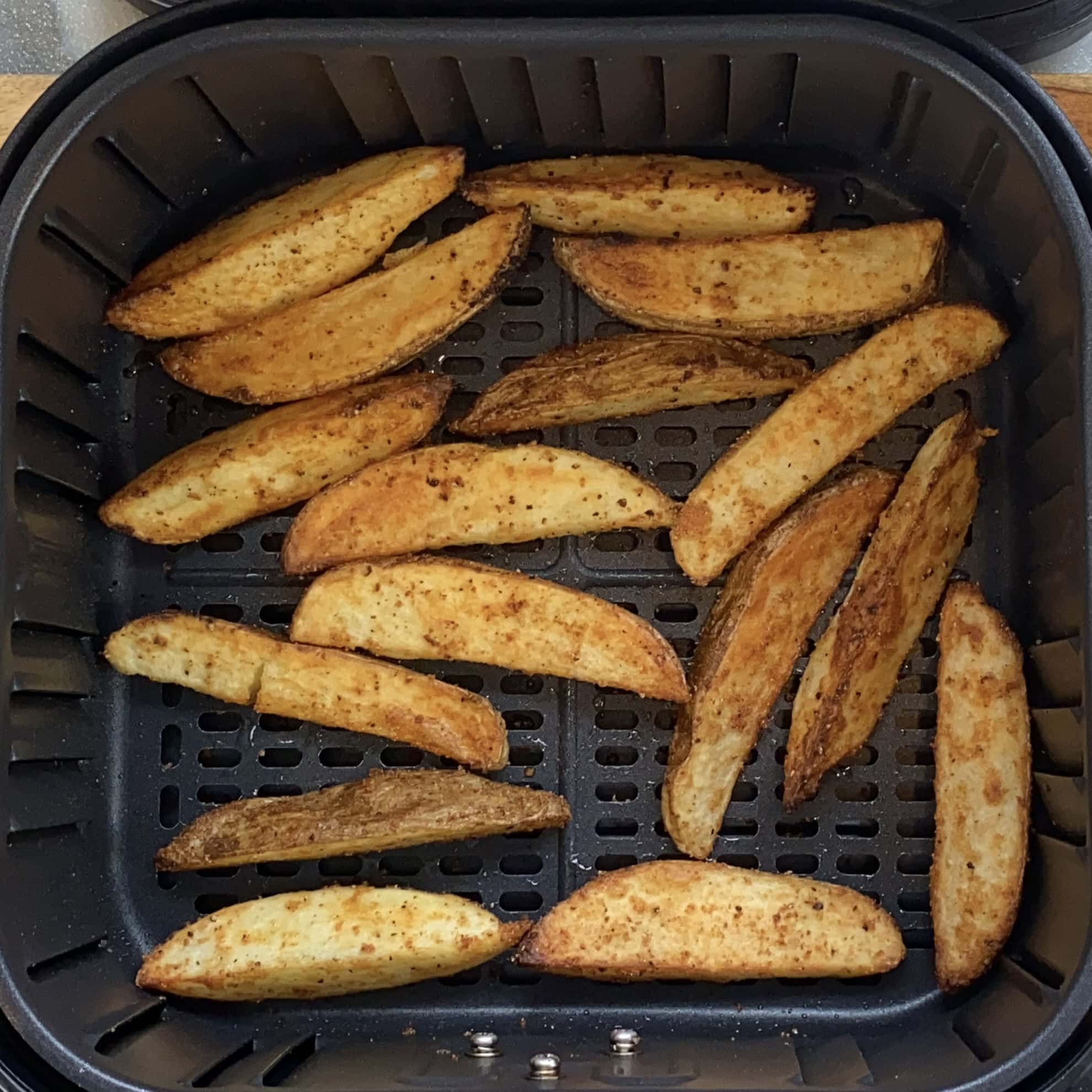 Potato wedges coated with seasoning are arranged in a single layer inside an air fryer basket.