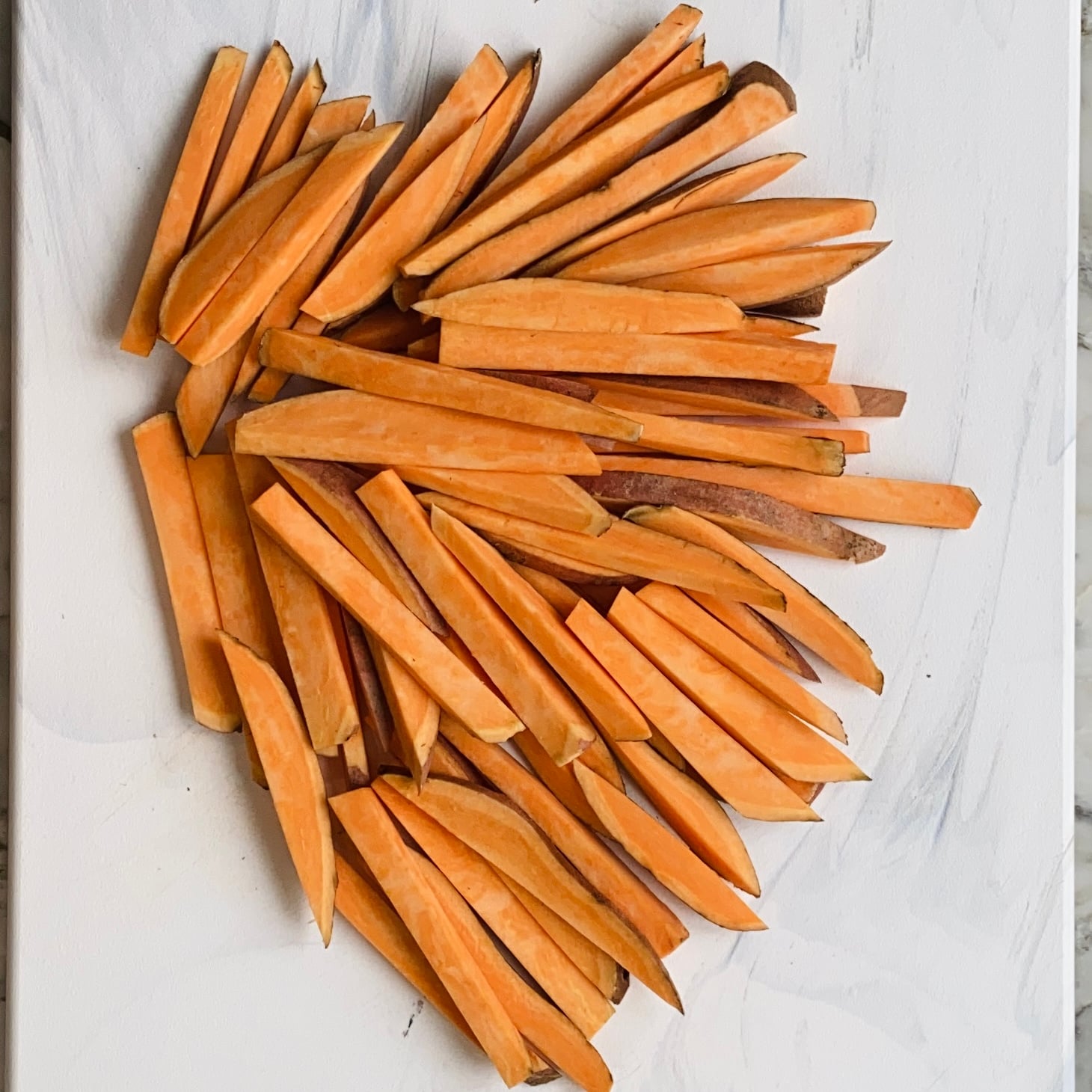 Raw sweet potato fries arranged in the shape of a heart on a white surface.