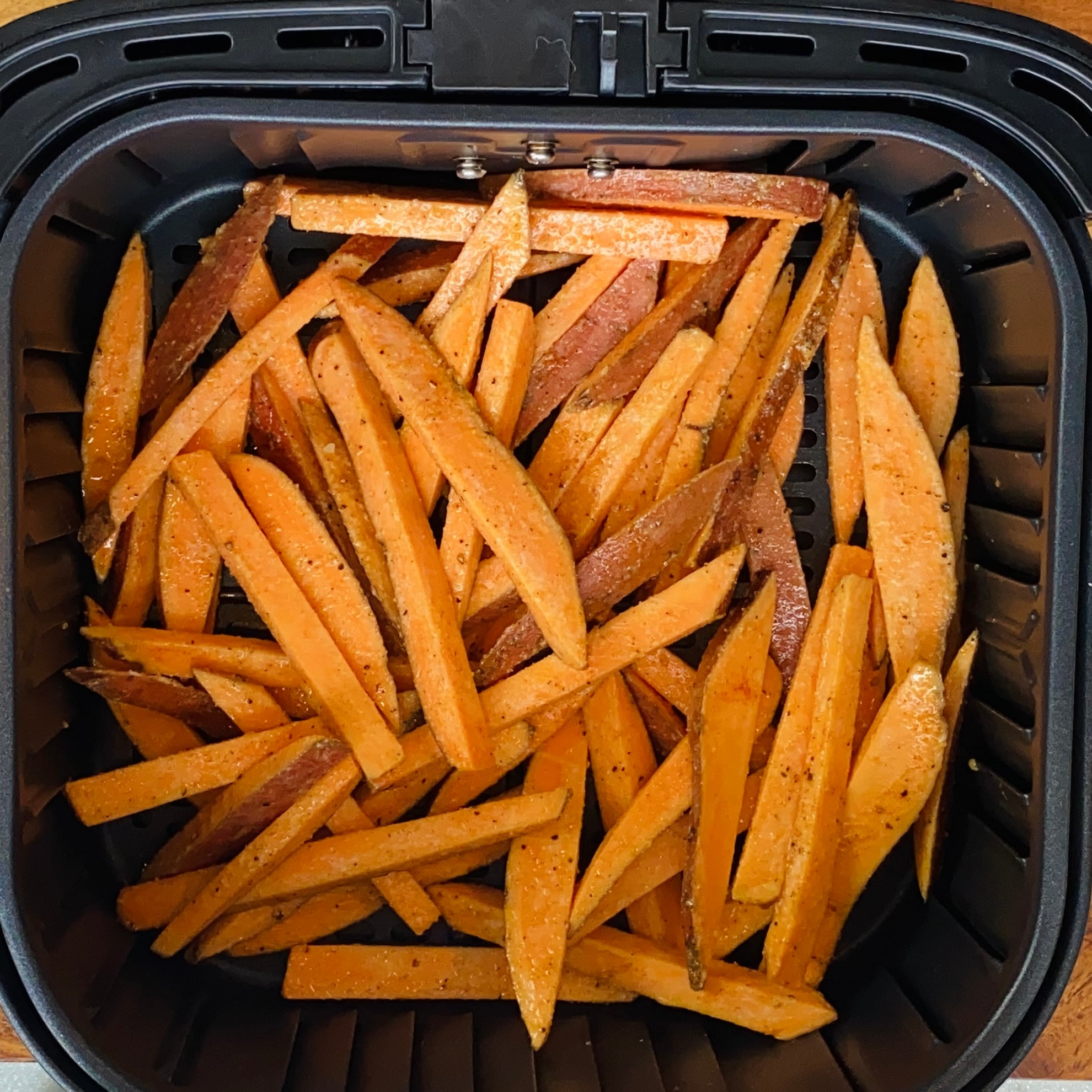 Seasoned sweet potato fries arranged in a single layer inside the basket of an air fryer, ready for cooking.