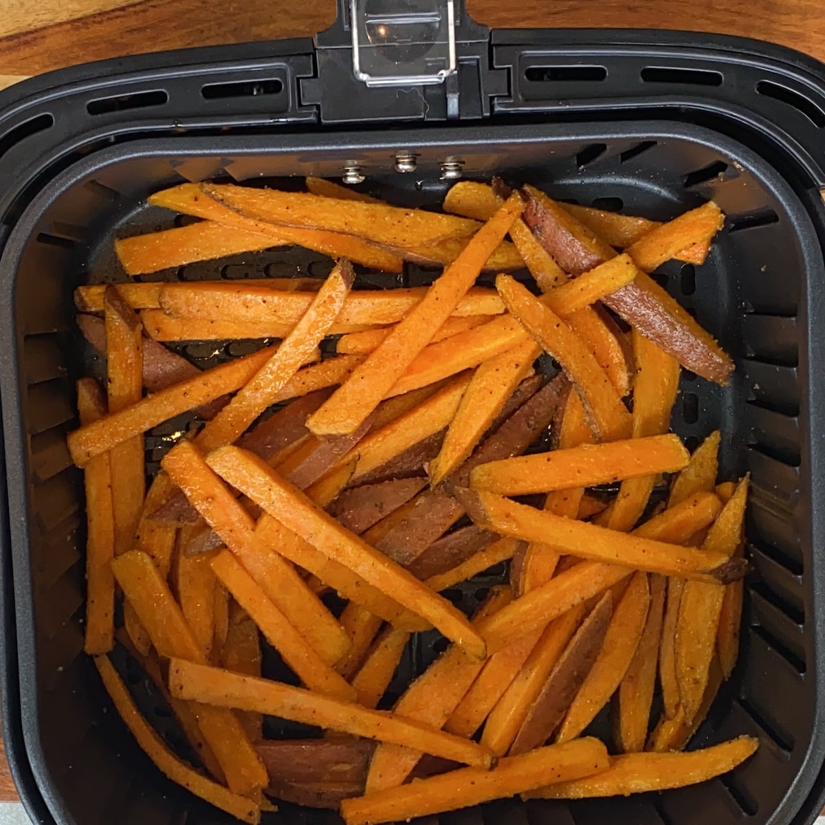 Sweet potato fries arranged in a single layer inside an air fryer basket, ready for or after cooking.