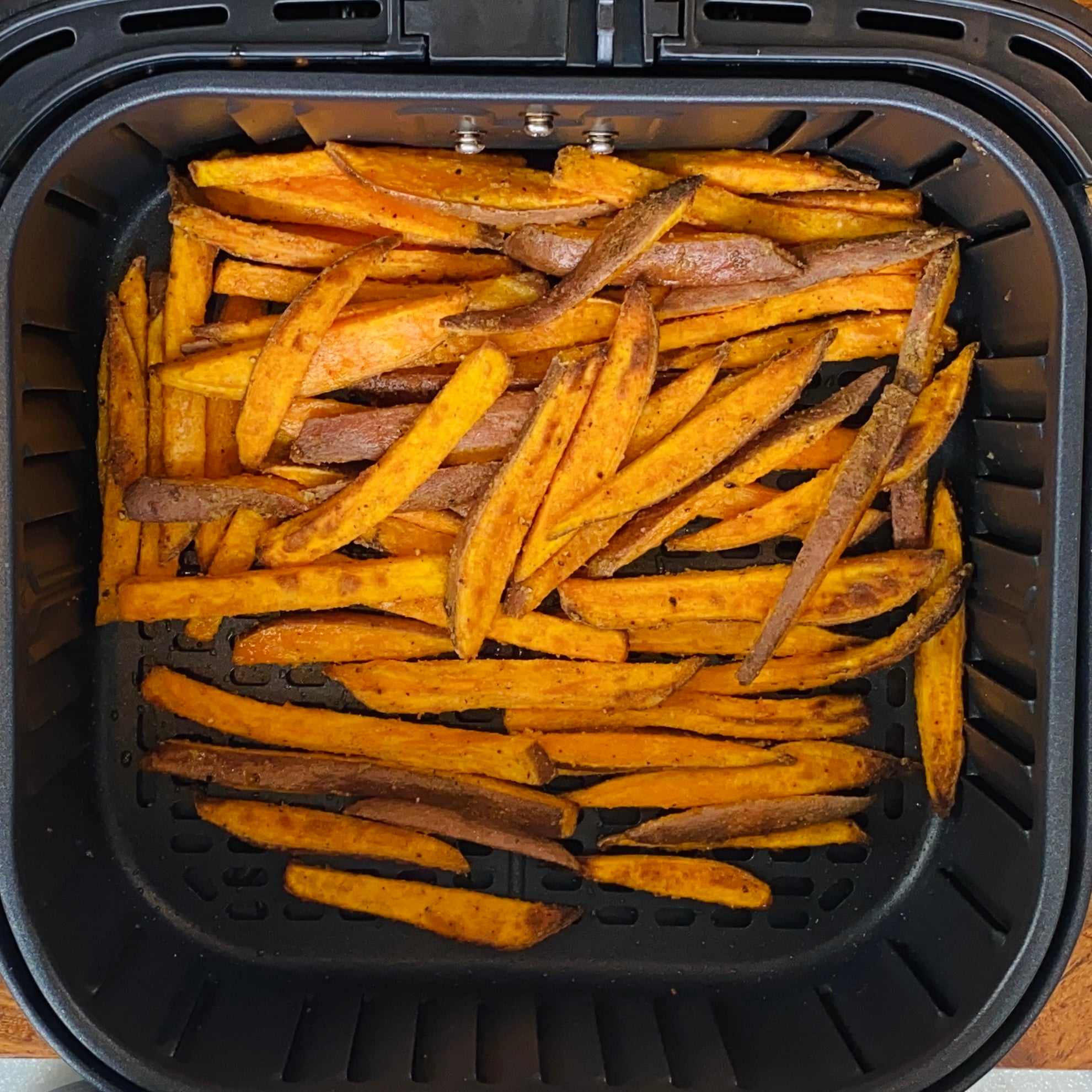 Sweet potato fries spread in a single layer inside an air fryer basket, cooked with seasoning visible on the surface.