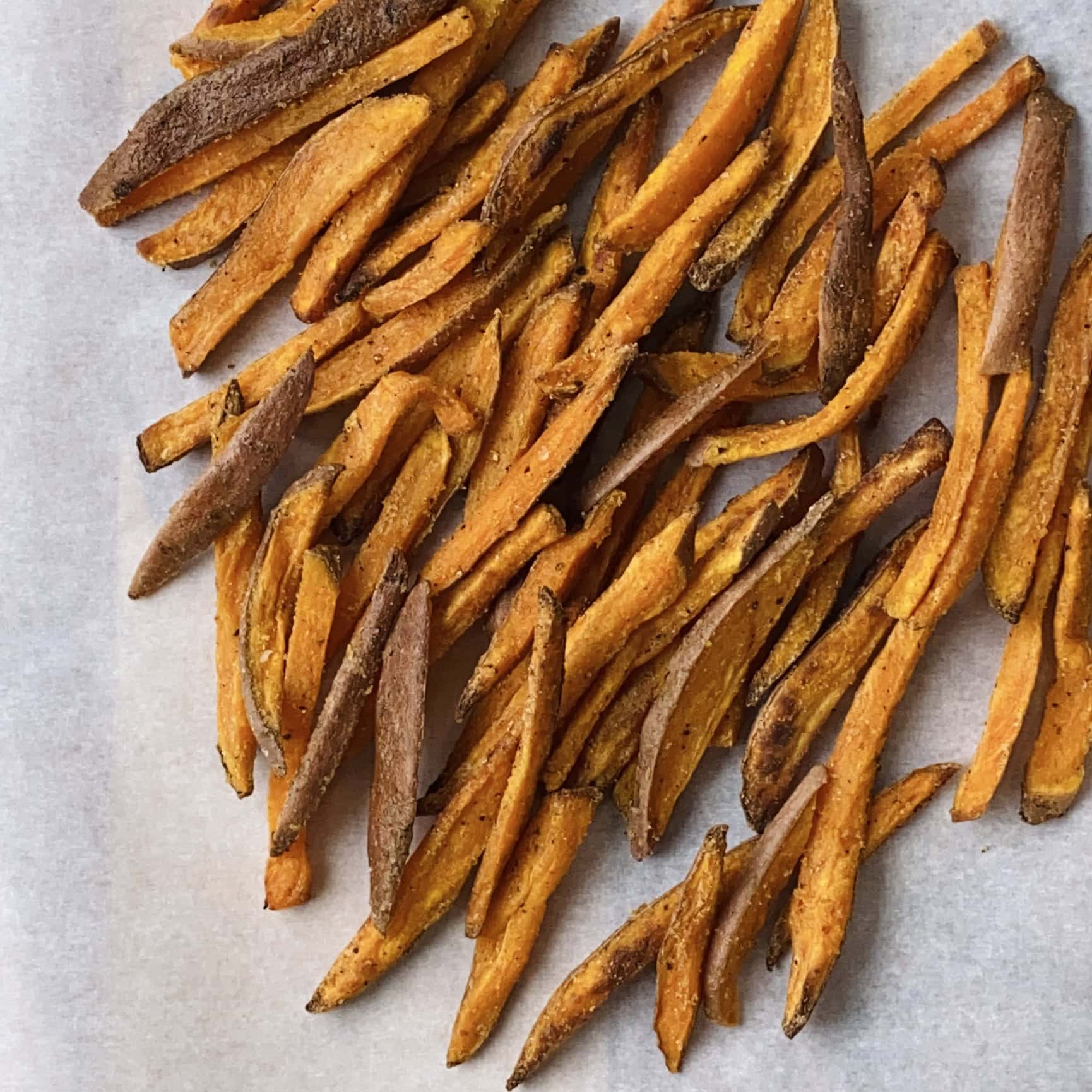 A pile of baked sweet potato fries arranged on a sheet of parchment paper.