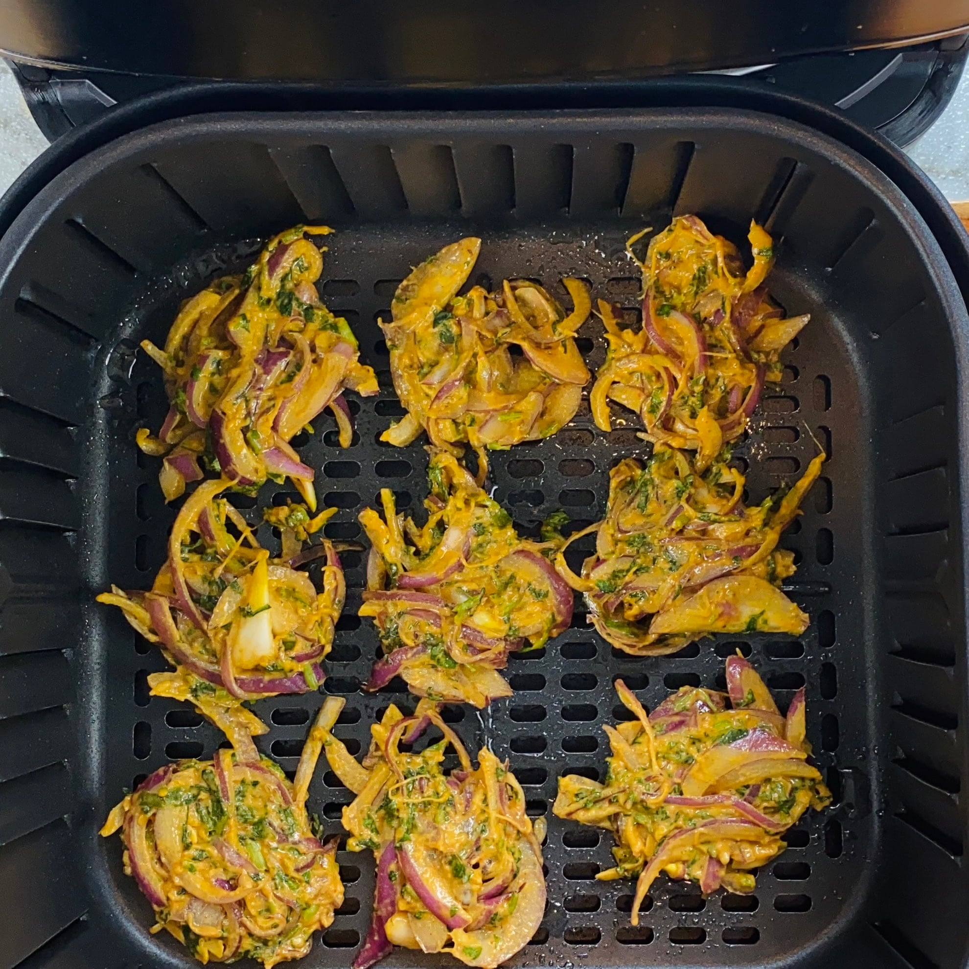 Uncooked vegetable fritters made with onions, herbs, and spices arranged in an air fryer basket, ready to be cooked.