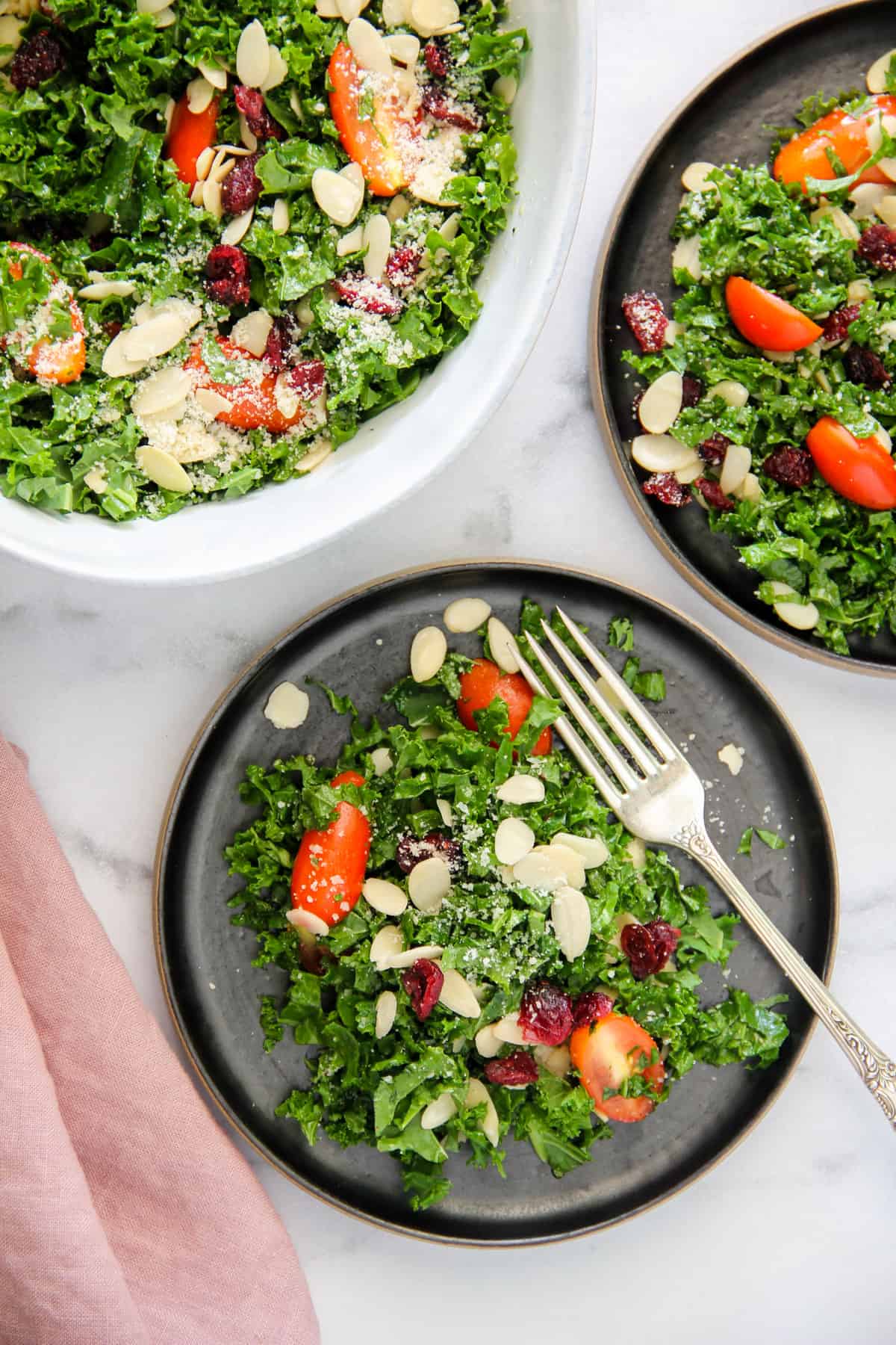 kale salad with almonds and cranberries served on a black plate 