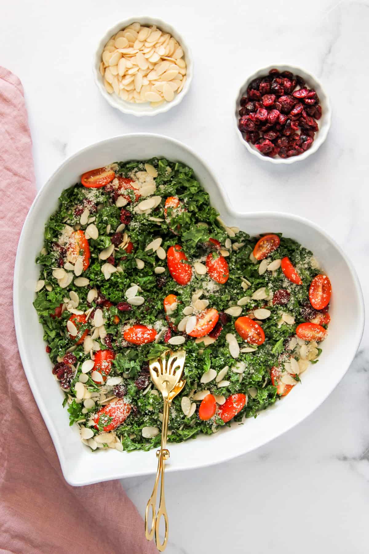 Kale salad in a heart shaped bowl with gold tongs
