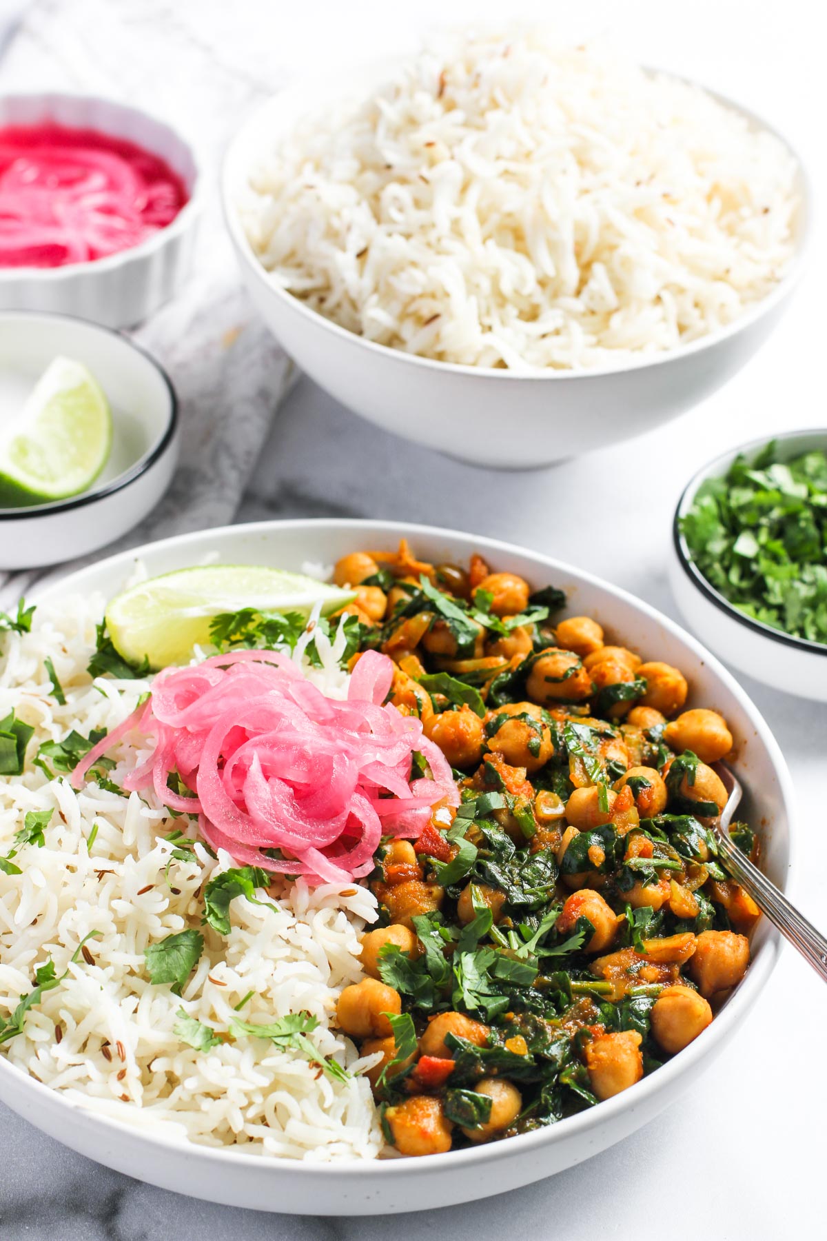 chana saag served in a white bowl with rice, pickled onions and lime wedge