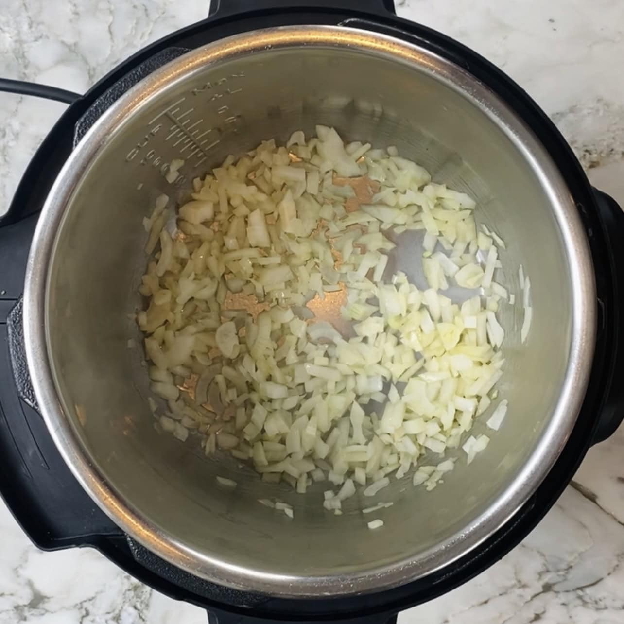 Chopped onions sautéing in an Instant Pot on a marble countertop.