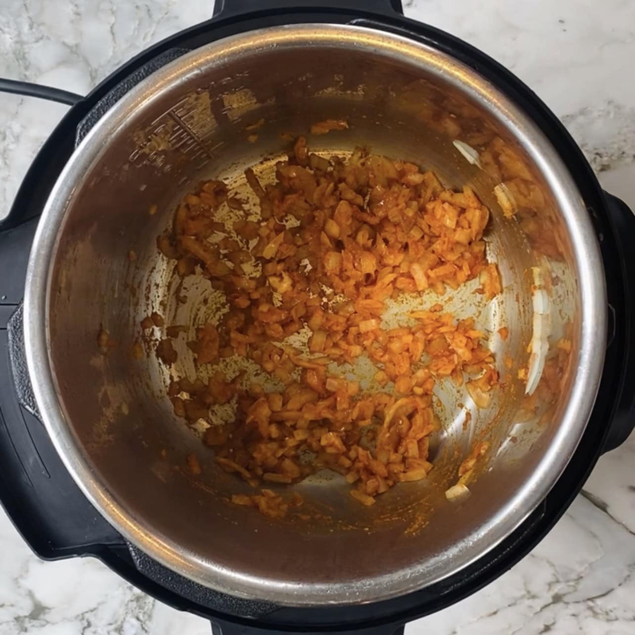 Chopped onions and spices sautéing in an Instant Pot on a marble countertop.