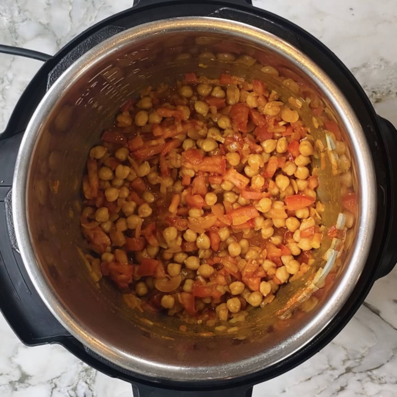 Chickpeas and chopped tomatoes in an Instant Pot on a marble countertop.