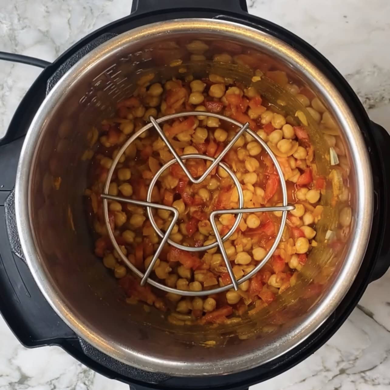 Chickpeas and diced tomatoes are cooked together in an Instant Pot, with a metal trivet placed on top of the mixture.