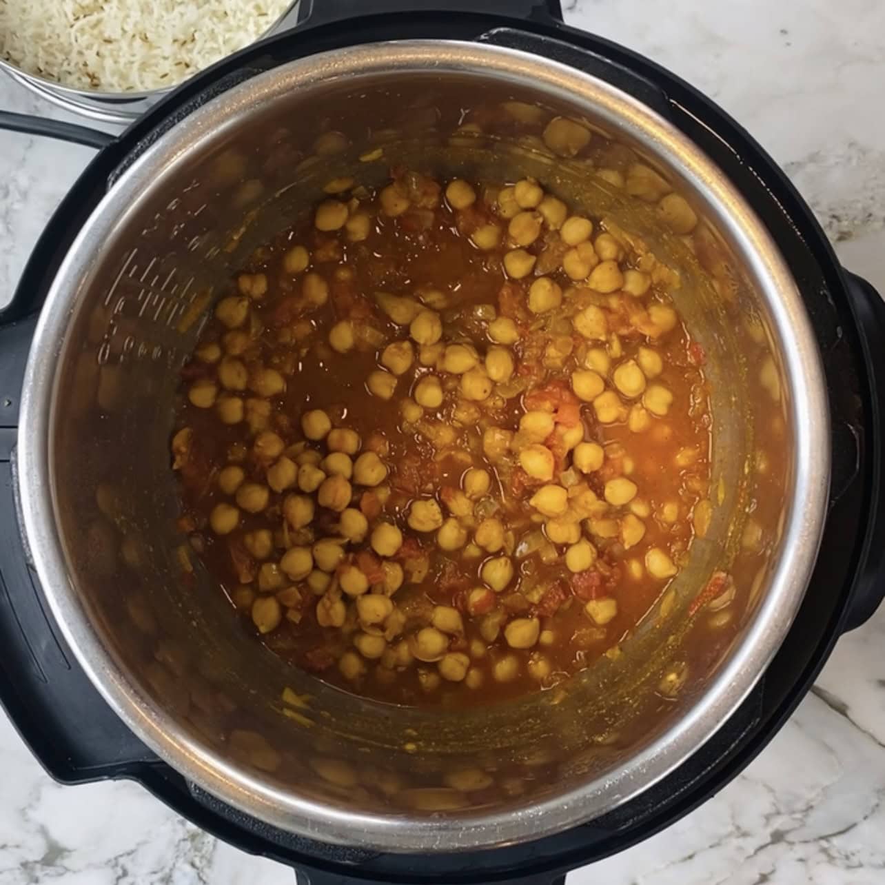 Instant Pot chana saag curry with tomatoes and spices, viewed from above on a marble countertop. A bowl of cooked rice is partially visible in the corner.
